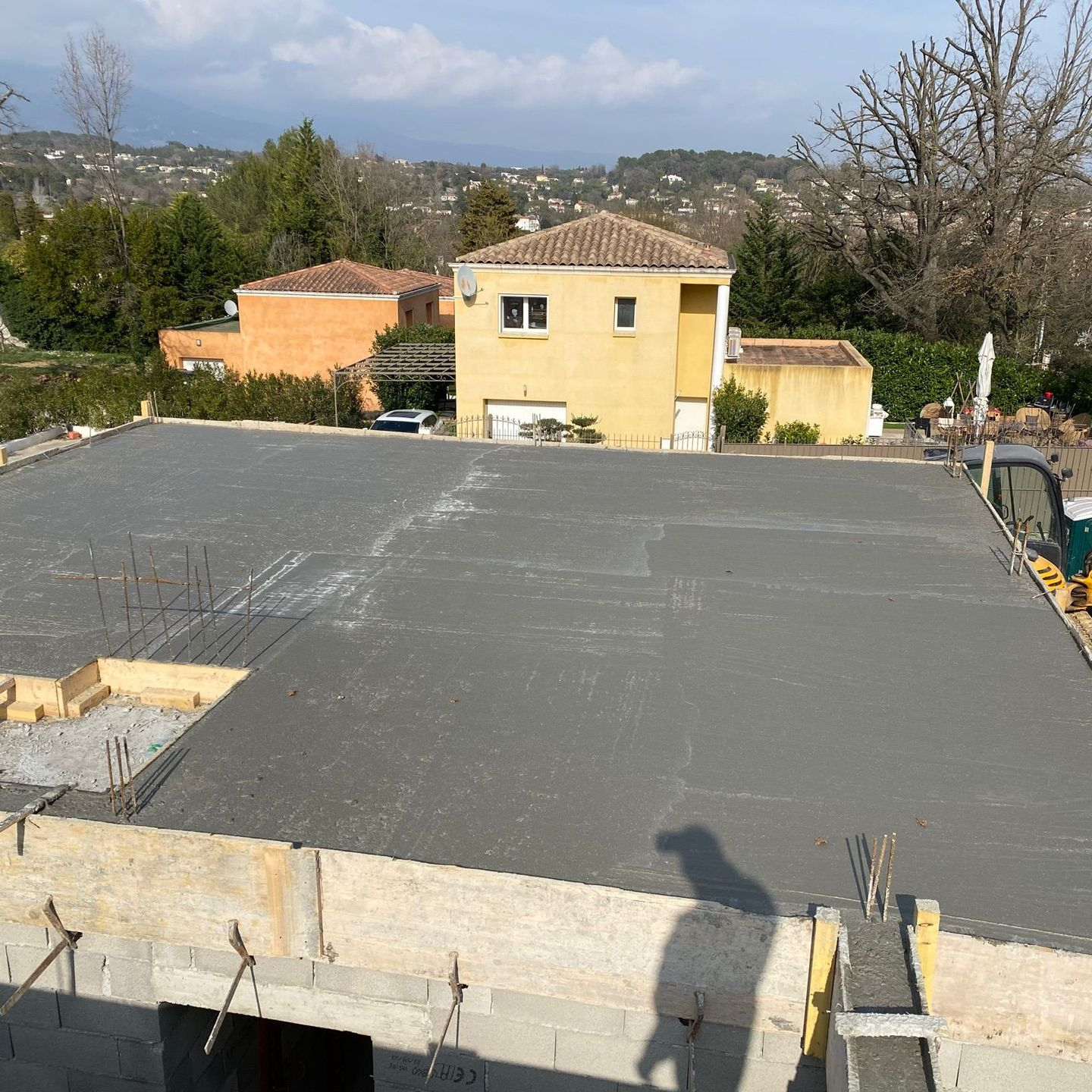Toit en béton fraîchement coulé, avec des maisons et des arbres en arrière-plan.