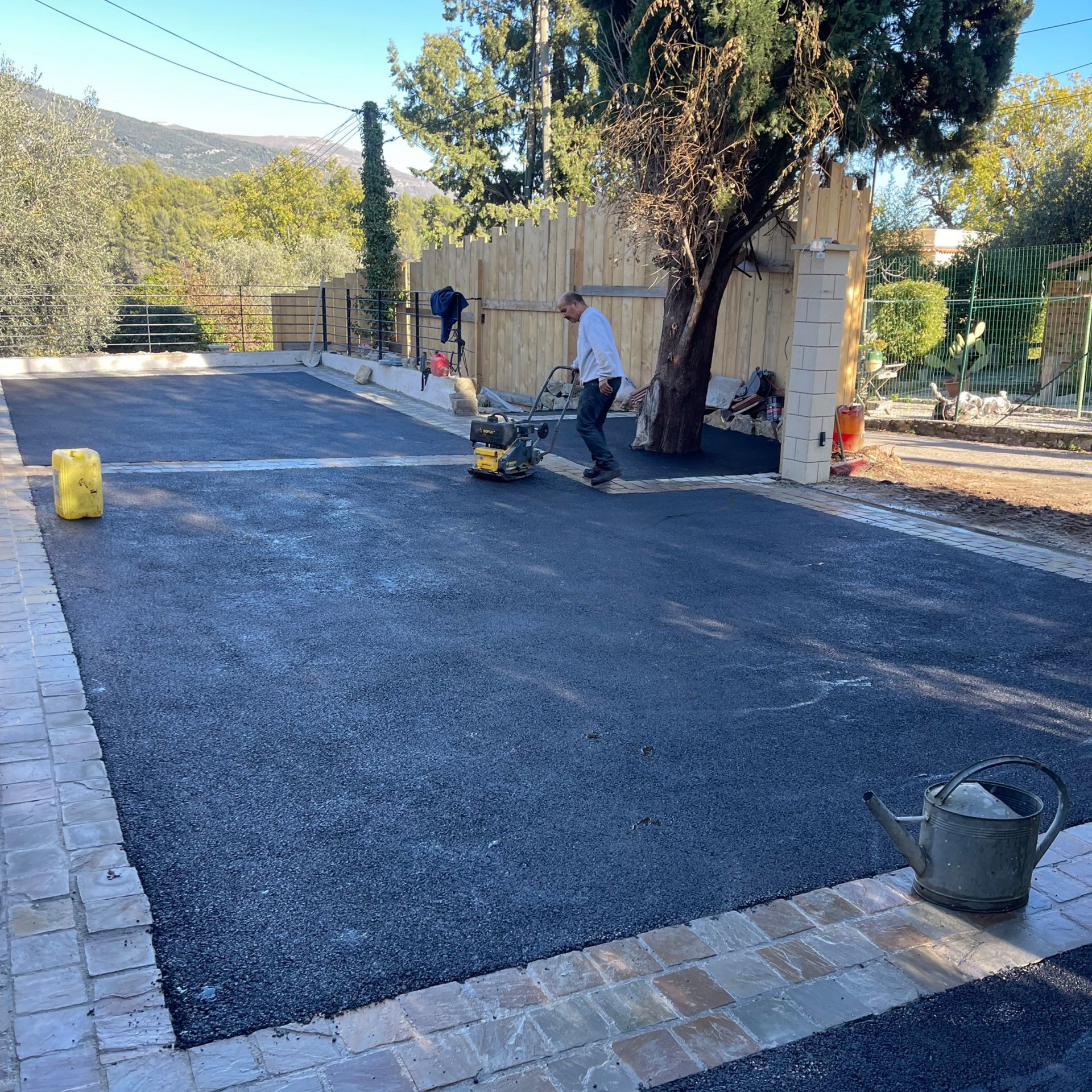 Sol extérieur en enrobé noir délimité par des pavés en pierre.