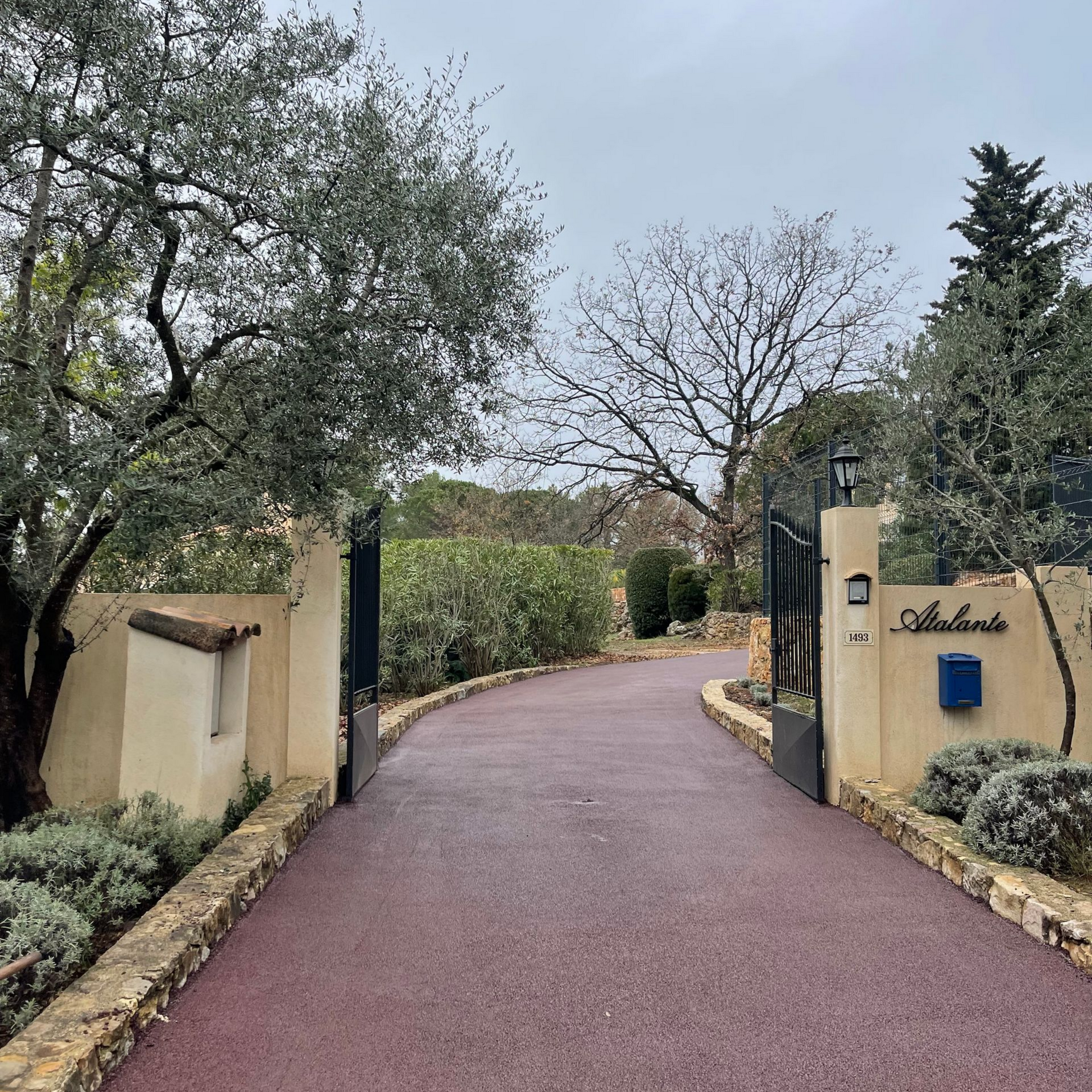 Entrée d'une propriété dont l'allée est en goudron rouge.