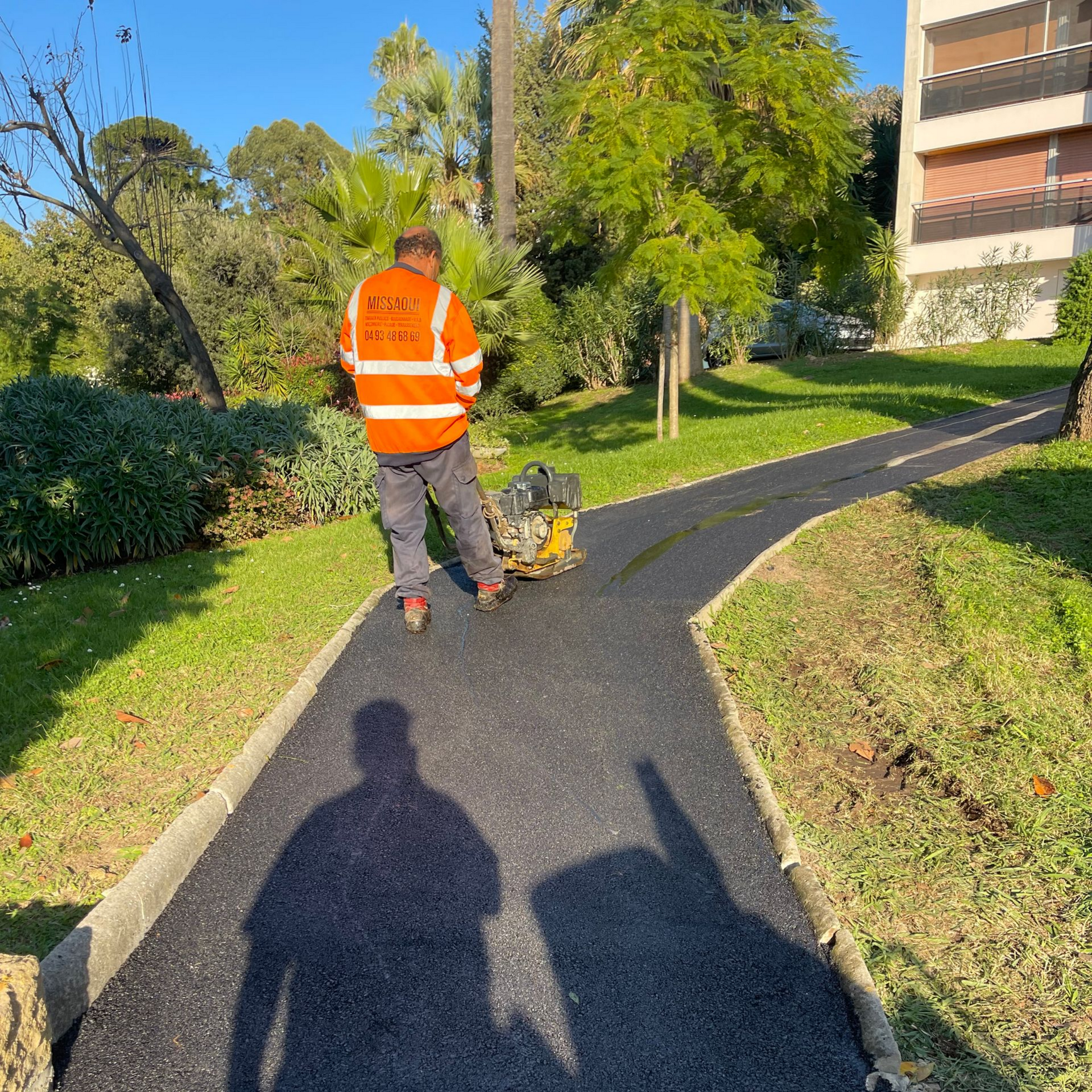 Un ouvrier aplanit un chemin fraîchement bitumé.