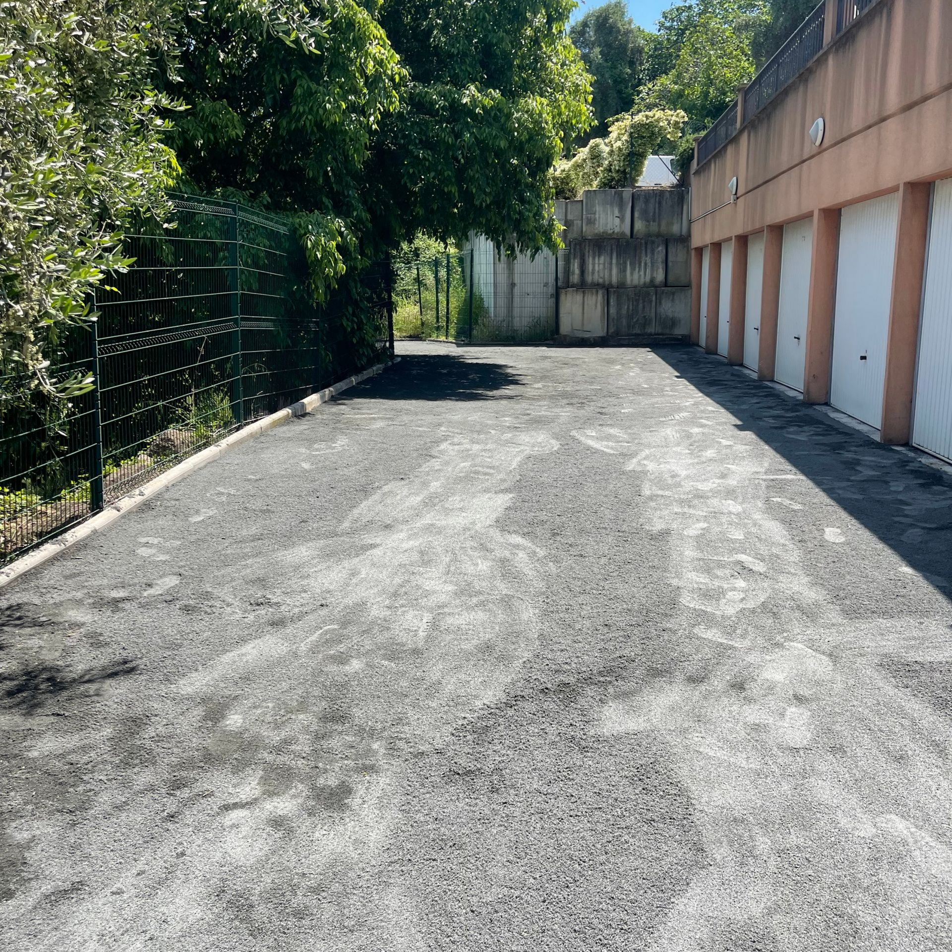 Aire de stationnement asphaltée avec des portes de garage à droite sur la gauche.
