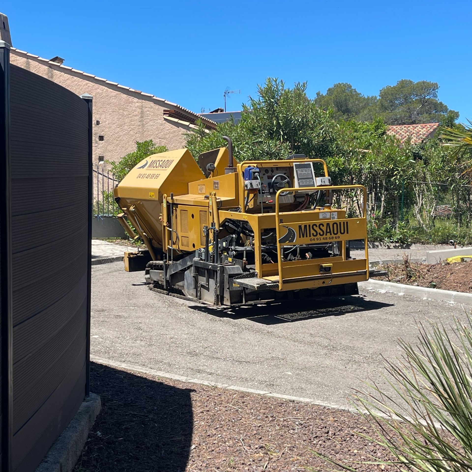 Machine à asphalte jaune sur un chemin de gravier.