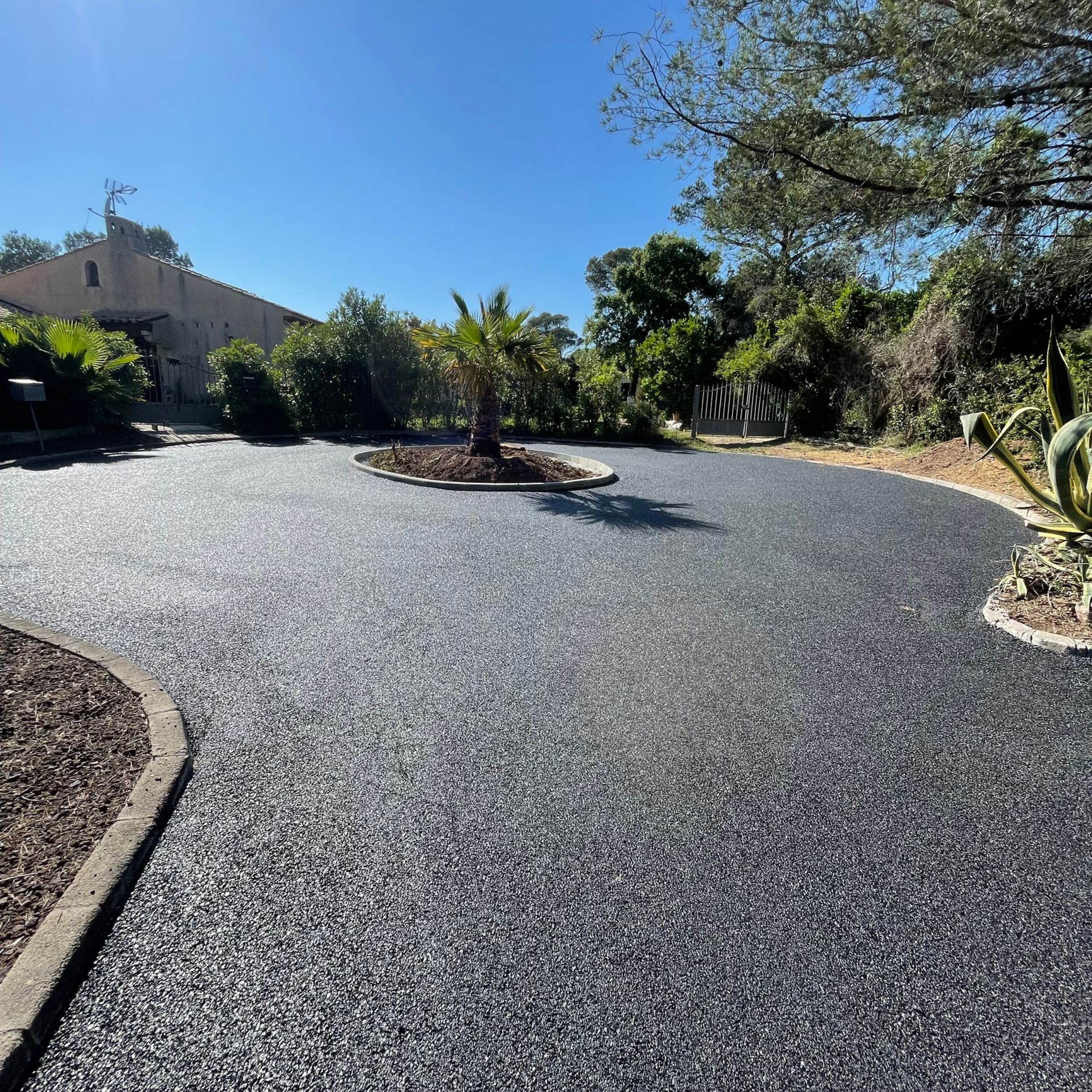 Allée en enrobé noir avec un îlot arboré au centre.