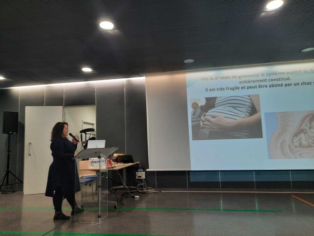 Une femme fait une présentation devant un écran de projection. Une photo d'un ventre de femme enceinte est affichée.