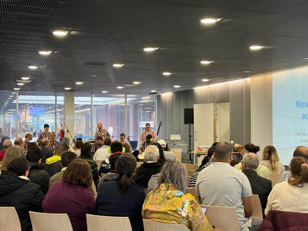 Un groupe de musique se produisant sur scène devant un public en intérieur, avec des textes projetés.