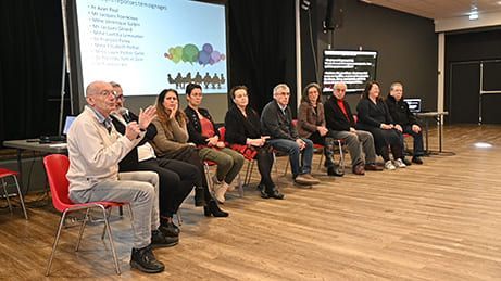 Un panel de personnes assises sur scène, un écran de présentation visible, quelques applaudissements.