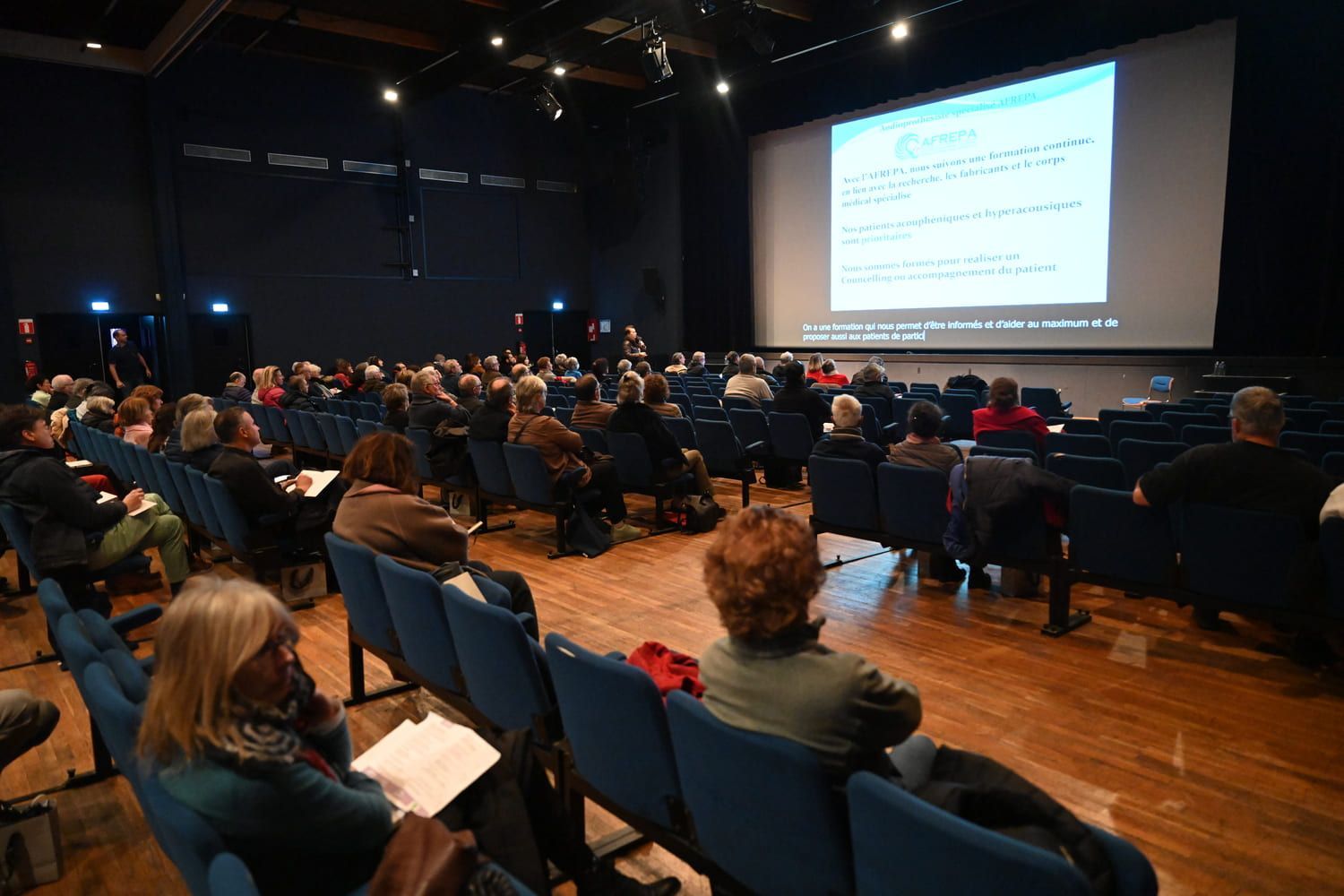 Dans un auditorium plongé dans l'obscurité, le public regarde une présentation sur un écran.