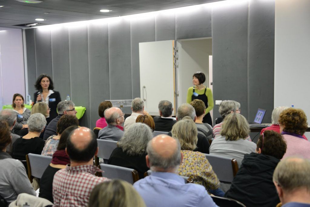 Deux femmes s'adressent à un public assis dans une salle de conférence.