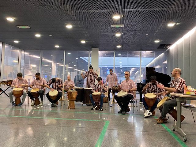 Un groupe joue de la batterie dans une pièce spacieuse. Les musiciens portent des chemises assorties, certains avec des instruments, d'autres à la batterie.