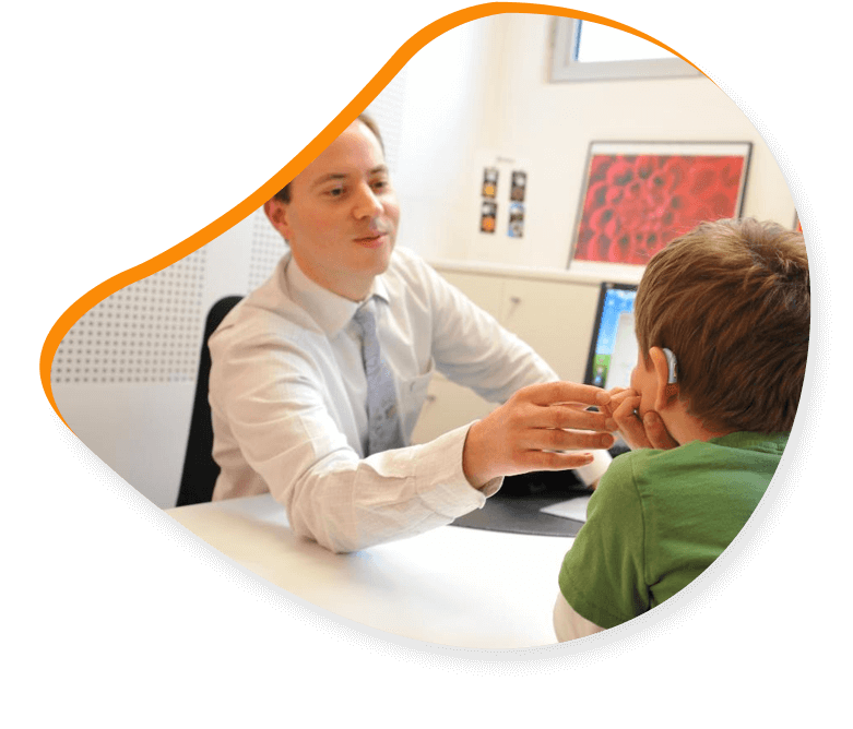Un audioprothésiste discute avec un enfant portant un appareil auditif dans son cabinet.