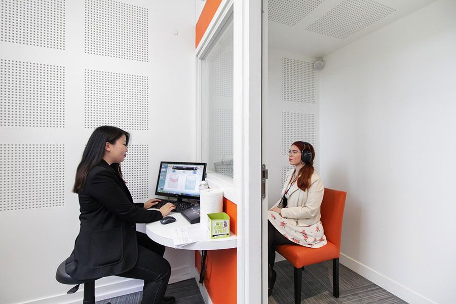 Une femme fait passer un test auditif à une autre femme dans des cabines insonorisées.