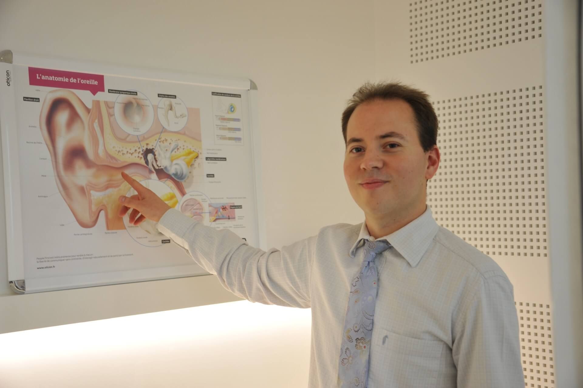 Un homme désigne un schéma de l'oreille, probablement pour expliquer l'anatomie de l'oreille dans un contexte médical.
