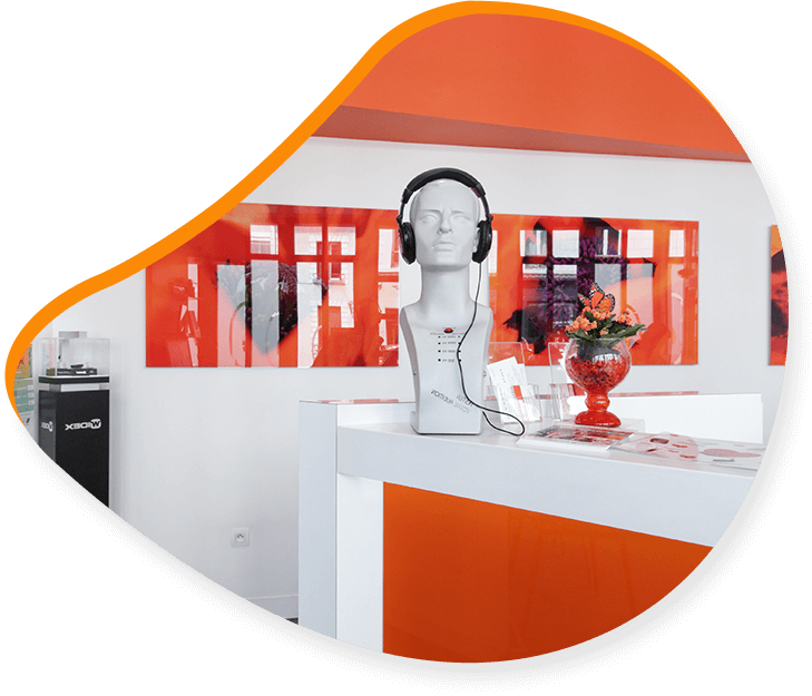 Un buste blanc portant un casque audio est posé sur un comptoir d'accueil blanc et orange, orné d'œuvres d'art et de fleurs.