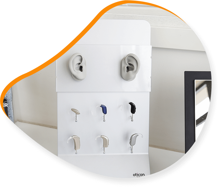 Vitrine blanche avec appareils auditifs, deux embouts auriculaires et une photo encadrée.