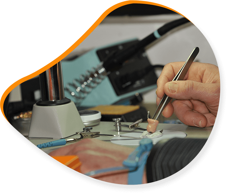 Main tenant une pince à épiler, travaillant sur un petit objet sur un établi, avec du matériel de soudure en arrière-plan.