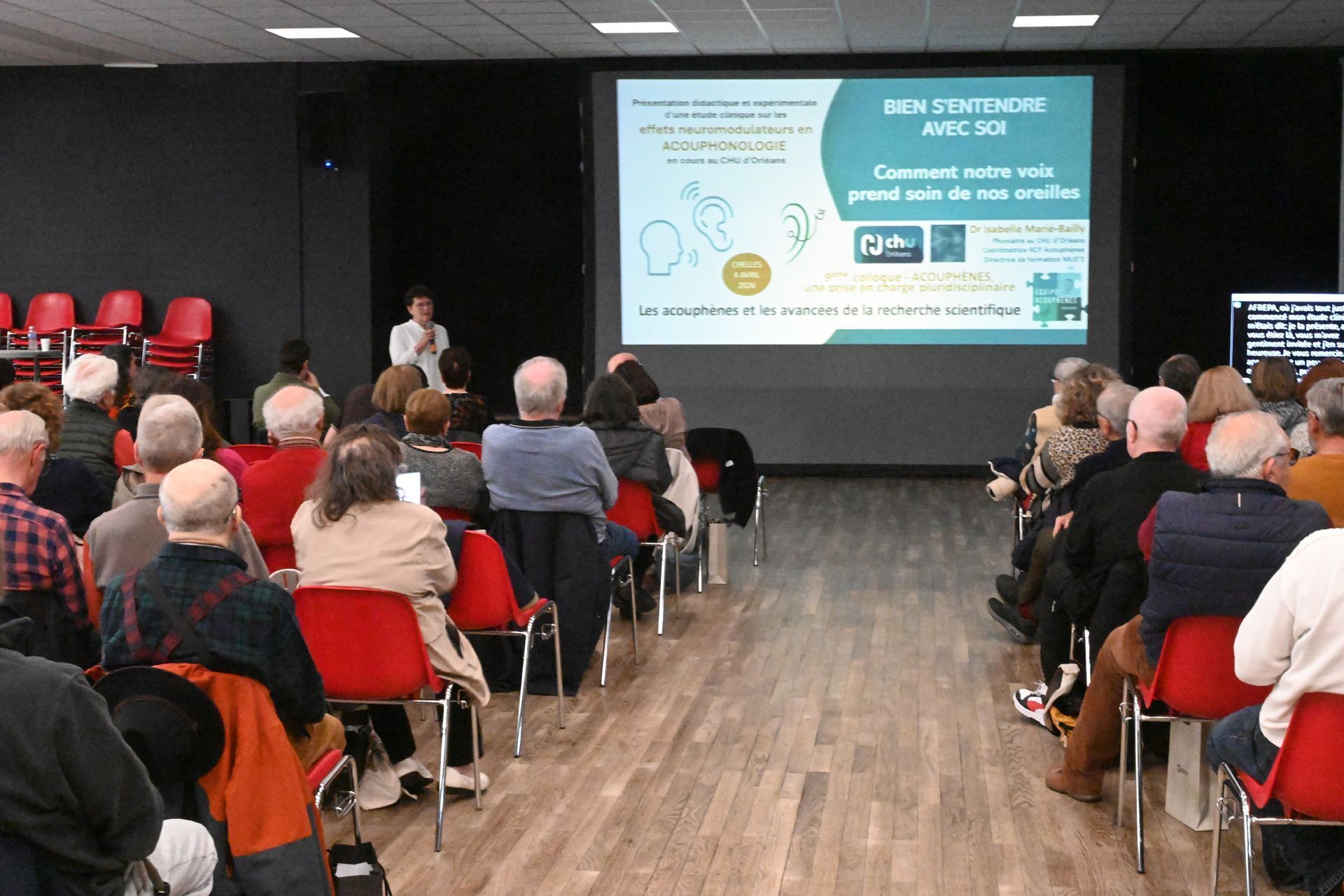 Public assis dans une salle, regardant une présentation sur grand écran