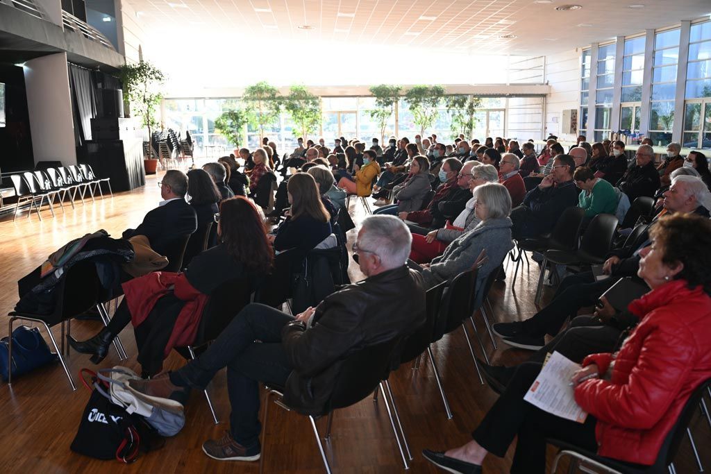 Le public est assis dans une grande salle, à l'écoute ; la lumière inonde la pièce.