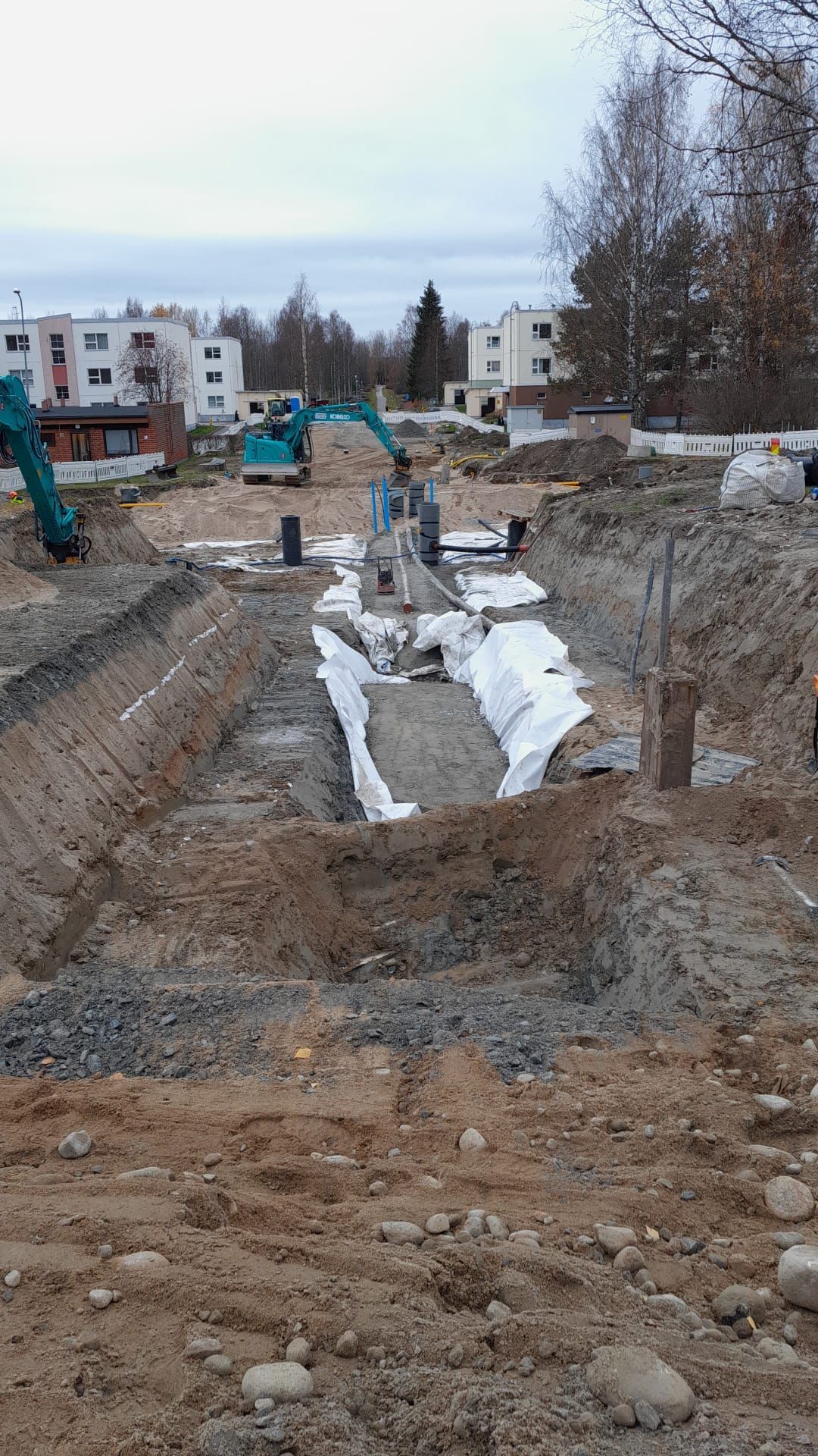 Työmaaoja kaivinkoneella, betonimuotteja ja lunta asuinkadun varrella
