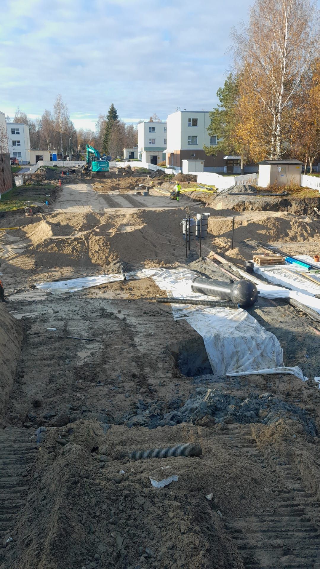 Rakennustyömaa, jossa on kaivettua maata, ojia ja pieni kaivinkone asuinalueella