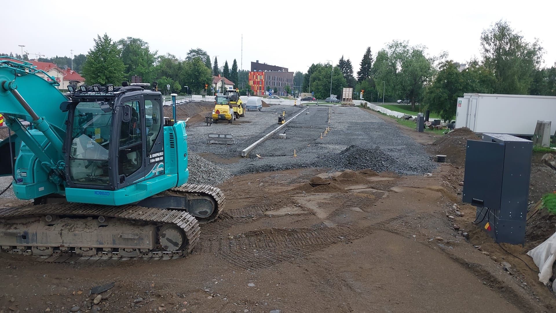 Turkoosi kaivinkone mutaisella rakennustyömaalla soratien ja maakasojen vieressä