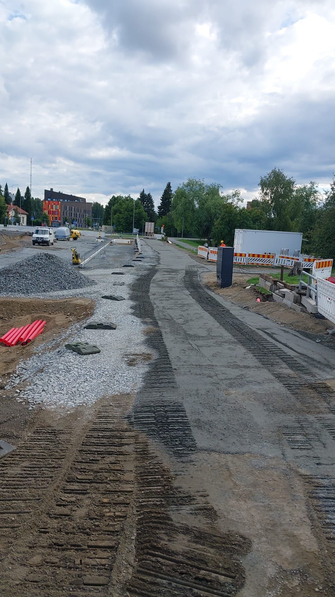 Tienrakennustyömaa, jossa on mutainen, keskeneräinen kaista, sorakasoja, barrikadeja ja pilvinen taivas