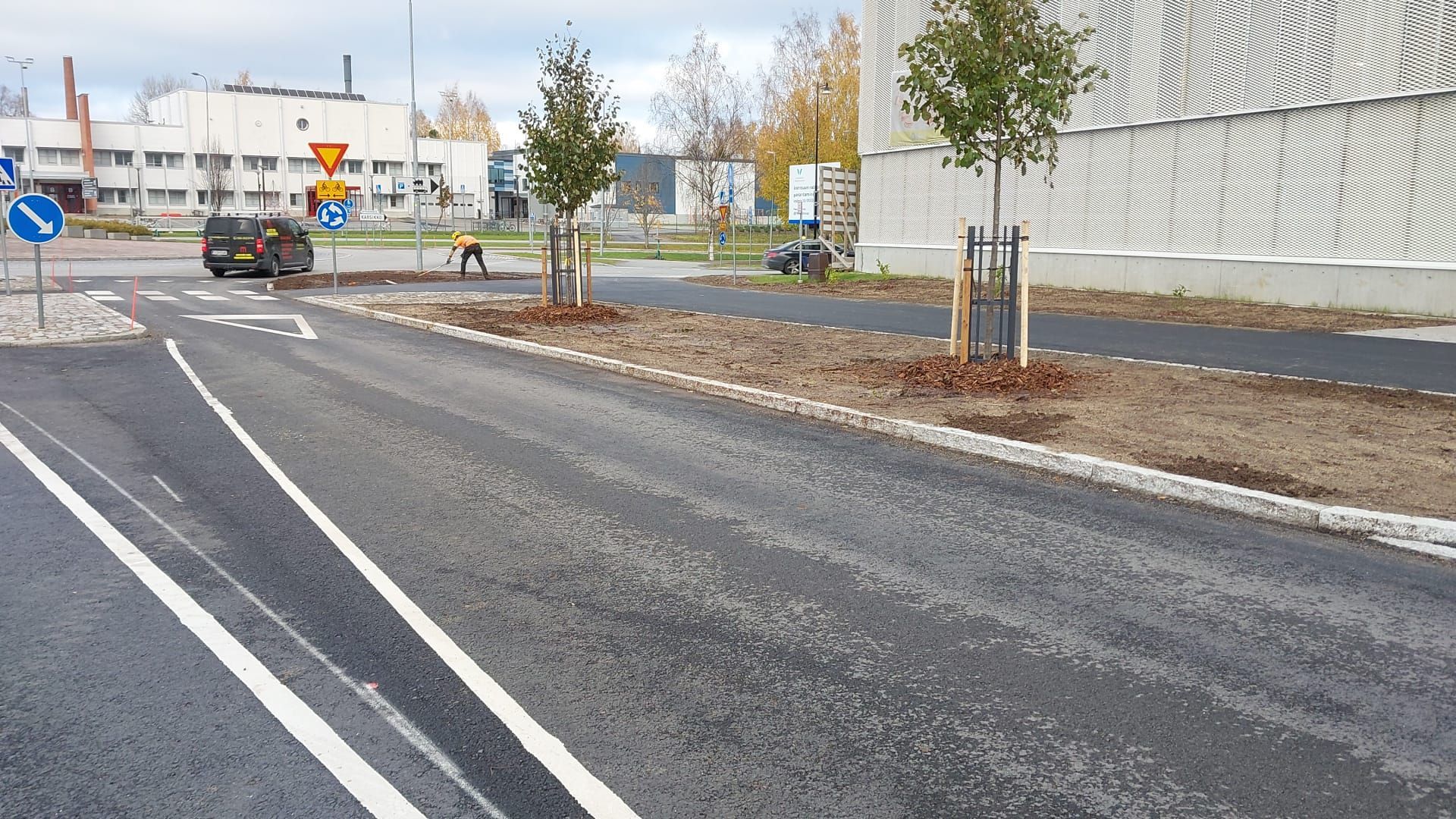 Hiljainen katu pyöräteillä, muutamalla autolla ja syksyisillä puilla aidatun tienvarsialueen lähellä