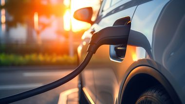 Câble de recharge pour voiture électrique branché sur un véhicule blanc, en extérieur au coucher du soleil.