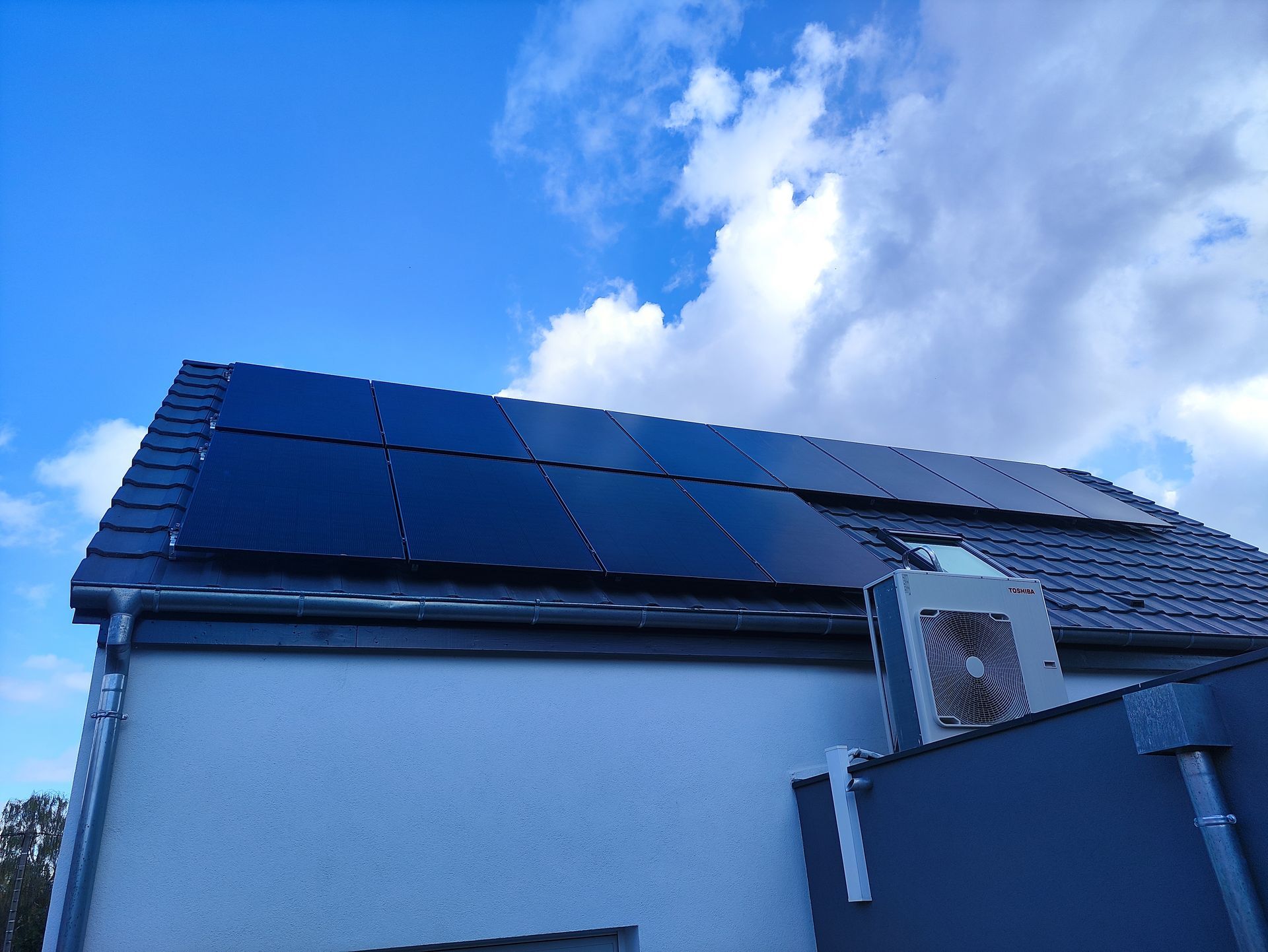 Des panneaux solaires sur un toit, sous un ciel bleu nuageux.