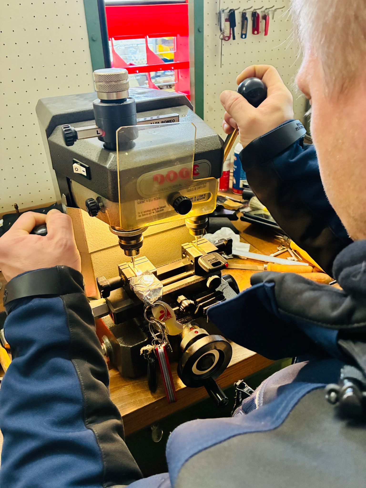 Eine Person bedient eine Schlüsselmaschine. Sie bedient die Maschine mit beiden Händen in einer Werkstattumgebung.