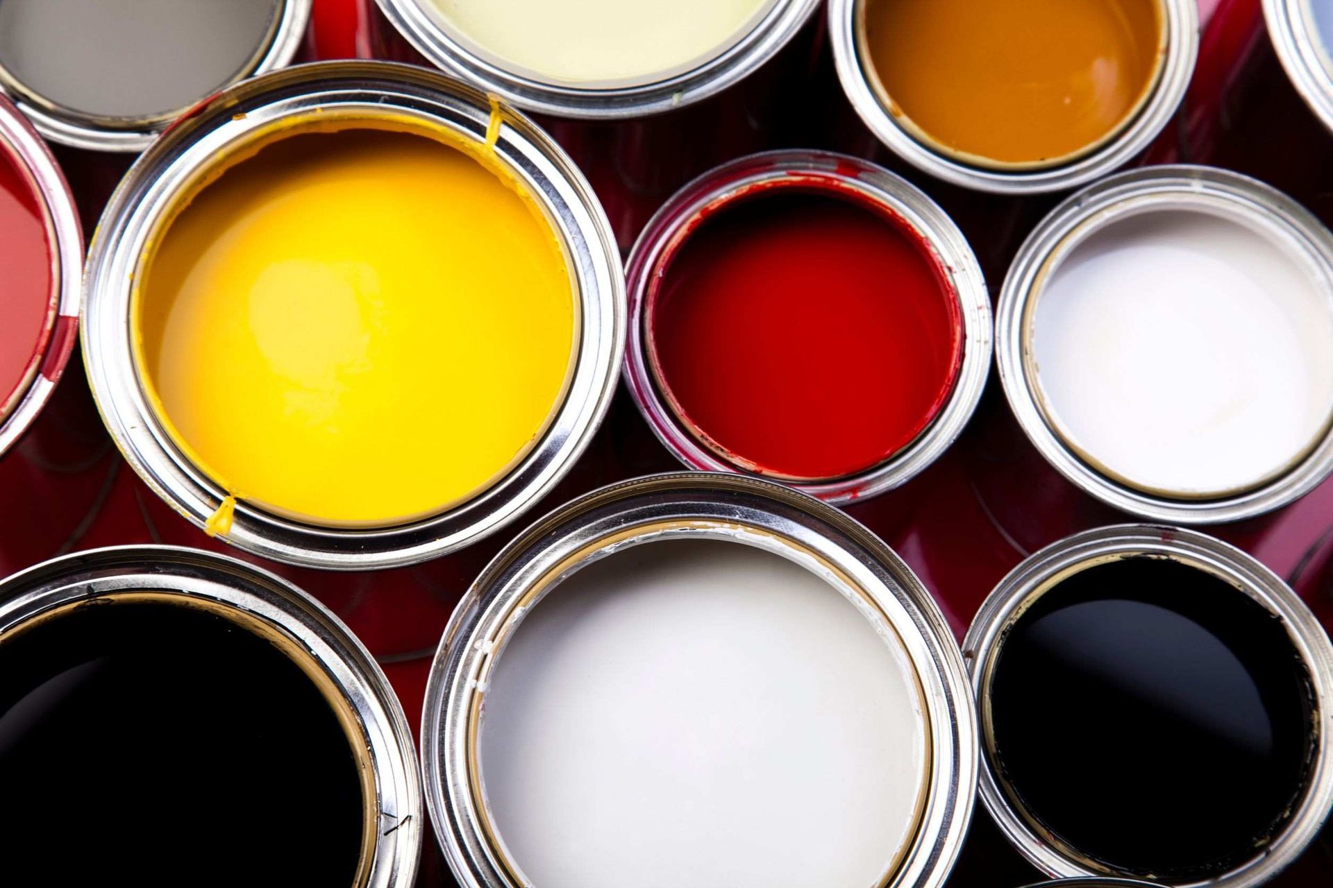 Latas de pintura abiertas de varios colores brillantes, incluidos amarillo, rojo, blanco y negro, vistas desde arriba.
