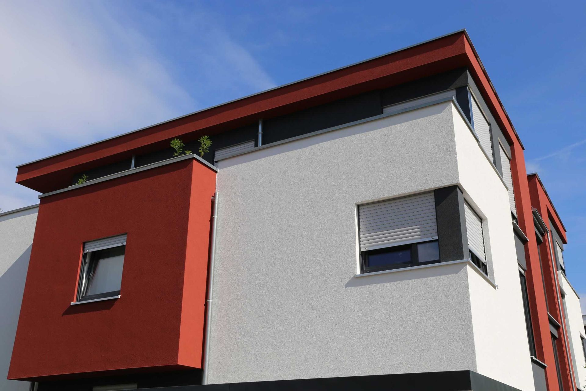 Edificio moderno de dos plantas con fachada en rojo y blanco. Cielo azul.