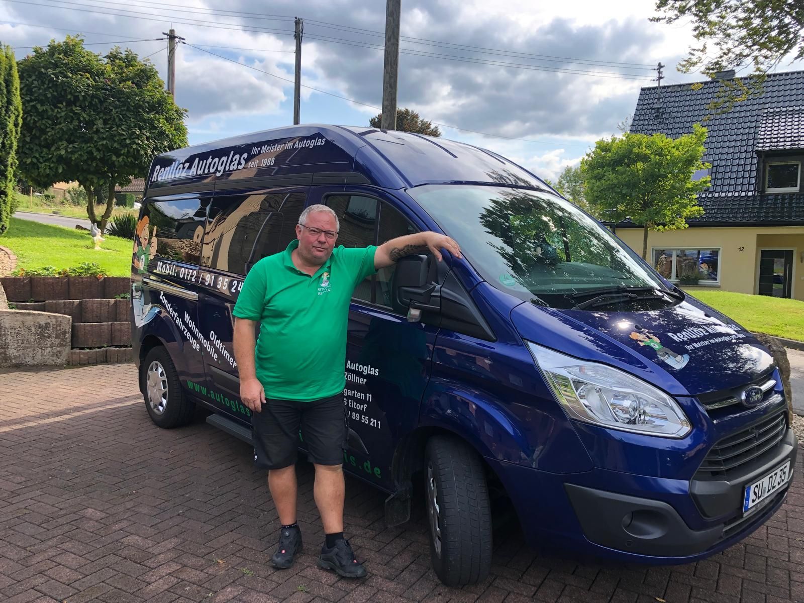 Ein Mann steht in einer Garage neben einem Auto mit geöffneter Motorhaube.