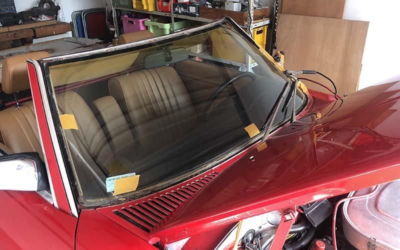 Ein rotes Auto mit kaputter Windschutzscheibe steht in einer Garage.