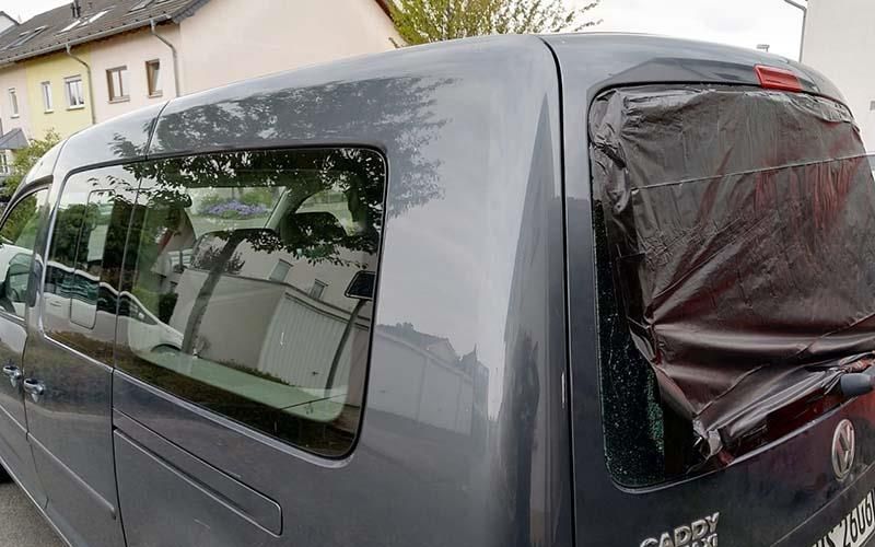 Ein grauer Lieferwagen mit zerbrochenem Fenster steht vor einem Haus.