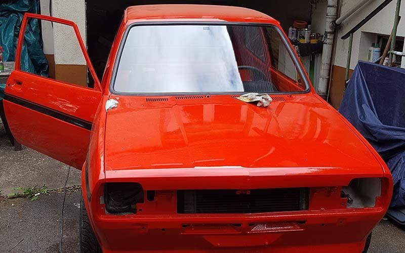 Ein rotes Auto mit offenen Türen steht vor einer Garage.
