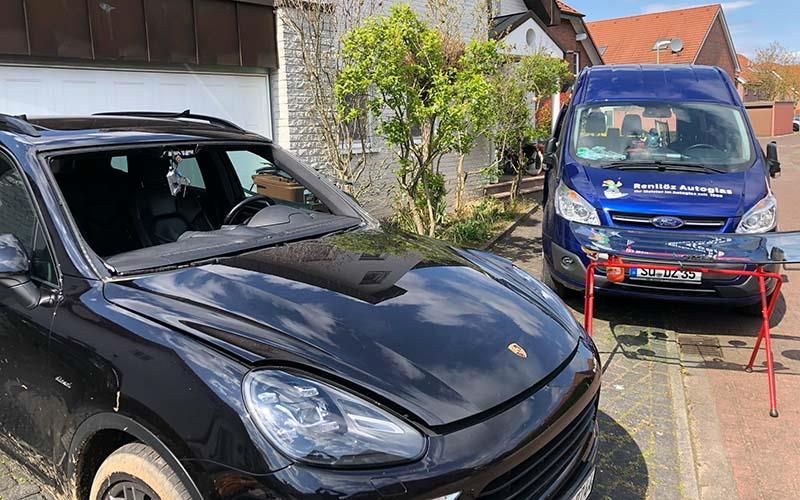 Ein schwarzes Auto mit kaputter Windschutzscheibe parkt neben einem blauen Lieferwagen.