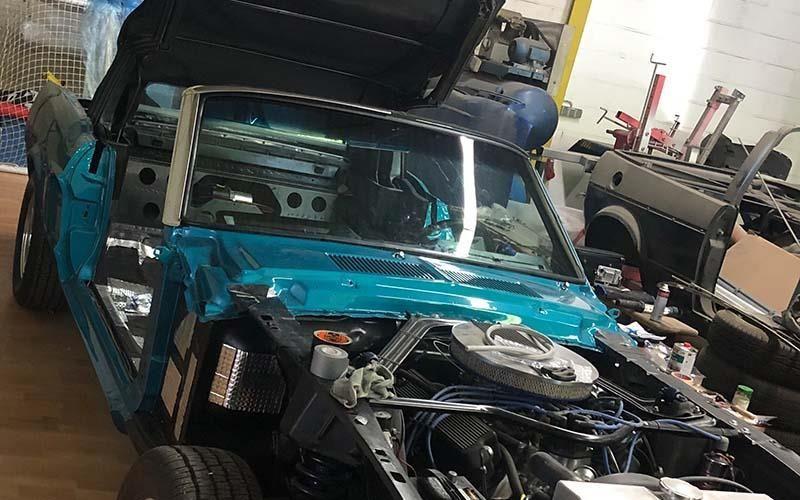 In einer Garage wird ein blaues Auto mit geöffnetem Verdeck gebaut.