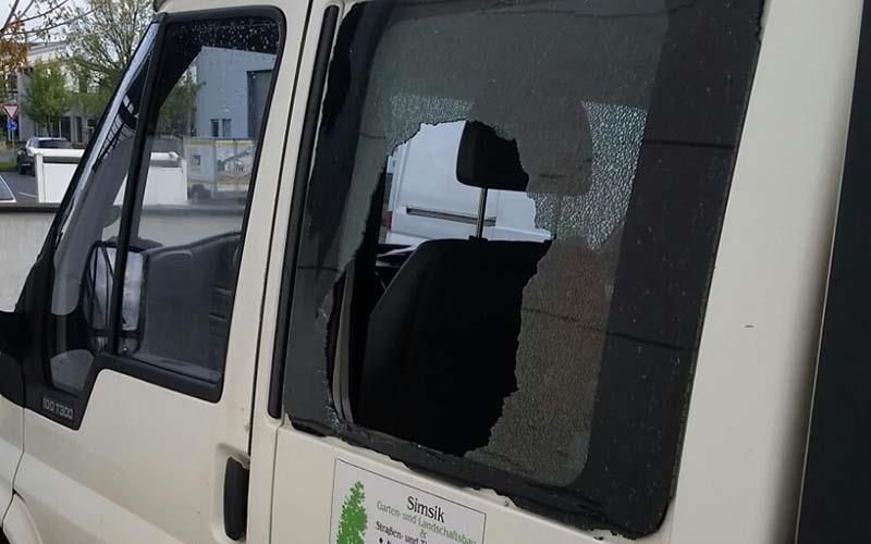 Auf einem Parkplatz steht ein weißer Lieferwagen mit zerbrochener Fensterscheibe.