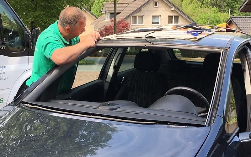 Ein Mann in einem grünen Hemd arbeitet an einer Windschutzscheibe eines Autos.