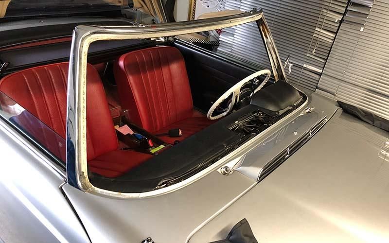 Ein silbernes Auto mit roten Sitzen und einem Lenkrad steht in einer Garage.