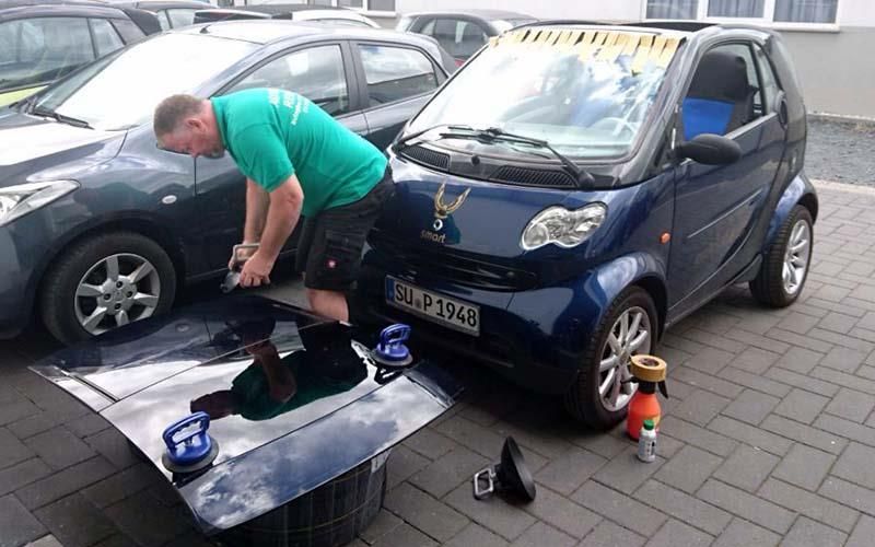Ein Mann im grünen Hemd poliert die Motorhaube eines blauen Autos