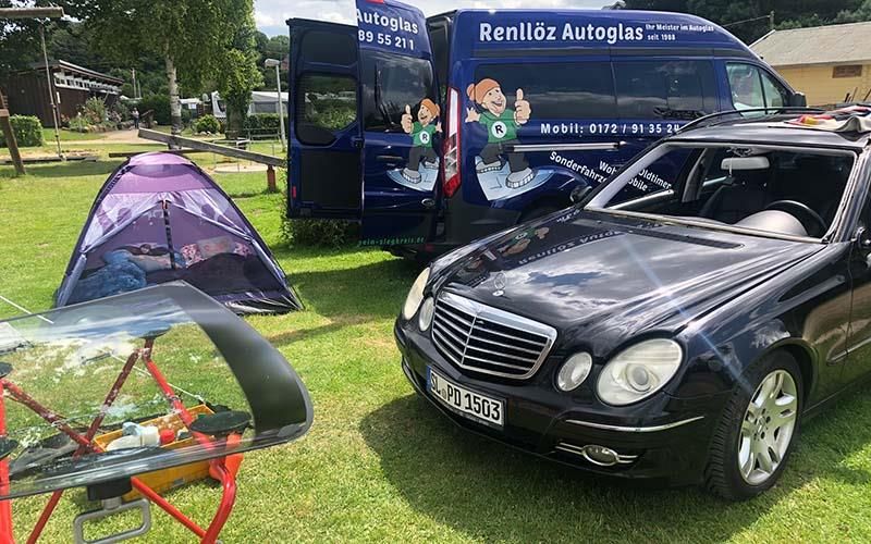 Auf einer Wiese parkt ein schwarzes Auto neben einem blauen Lieferwagen.