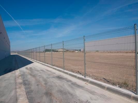 Una valla metálica rodea un gran campo vacío.