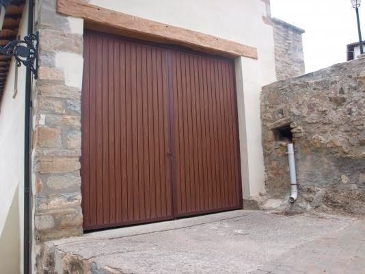 Una puerta de garaje marrón está colocada en el costado de un edificio, al lado de una pared de piedra.