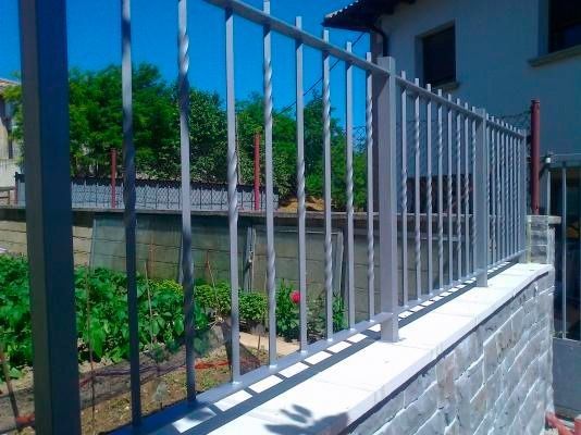 Una valla de metal rodea una pared de ladrillos delante de una casa.