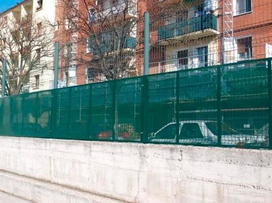 Una valla verde rodea un muro de hormigón delante de un edificio.