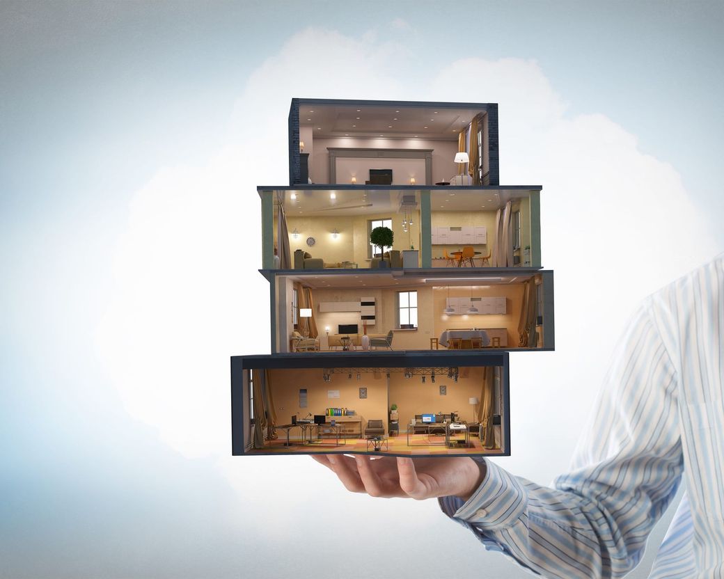 Mano sosteniendo una maqueta seccionada apilada de una casa moderna de varias plantas con las habitaciones iluminadas