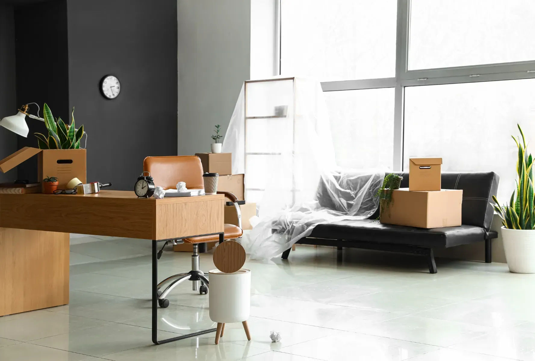 Una habitación con un escritorio, una silla, un sofá y cajas dentro.