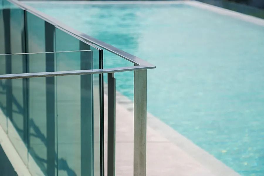 Un primer plano de una barandilla de vidrio junto a una piscina.