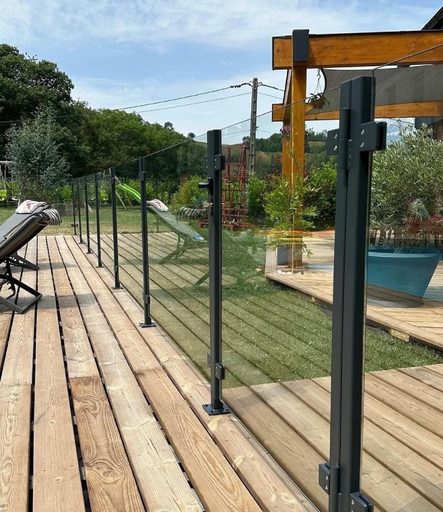 Una terraza de madera con barandilla de cristal y sillas encima.